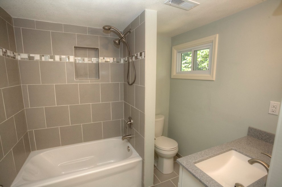 Photo of a mid-sized transitional bathroom in Kansas City with an alcove tub, a shower/bathtub combo, a two-piece toilet, gray tile, porcelain tile, green walls, porcelain floors, an undermount sink and laminate benchtops.