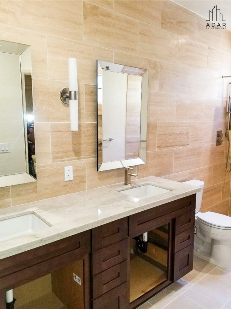 This is an example of a transitional 3/4 bathroom in Los Angeles with dark wood cabinets, an alcove shower, beige tile, stone tile, granite benchtops and white benchtops.