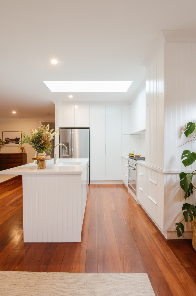 Mid-sized contemporary l-shaped kitchen in Perth with a double-bowl sink, white cabinets, white splashback, stainless steel appliances, with island, orange floor, white benchtop and flat-panel cabinets.