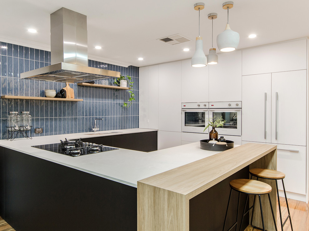 Contemporary u-shaped kitchen in Perth with an undermount sink, flat-panel cabinets, white cabinets, wood benchtops, blue splashback, panelled appliances, medium hardwood floors, a peninsula, brown floor and white benchtop.