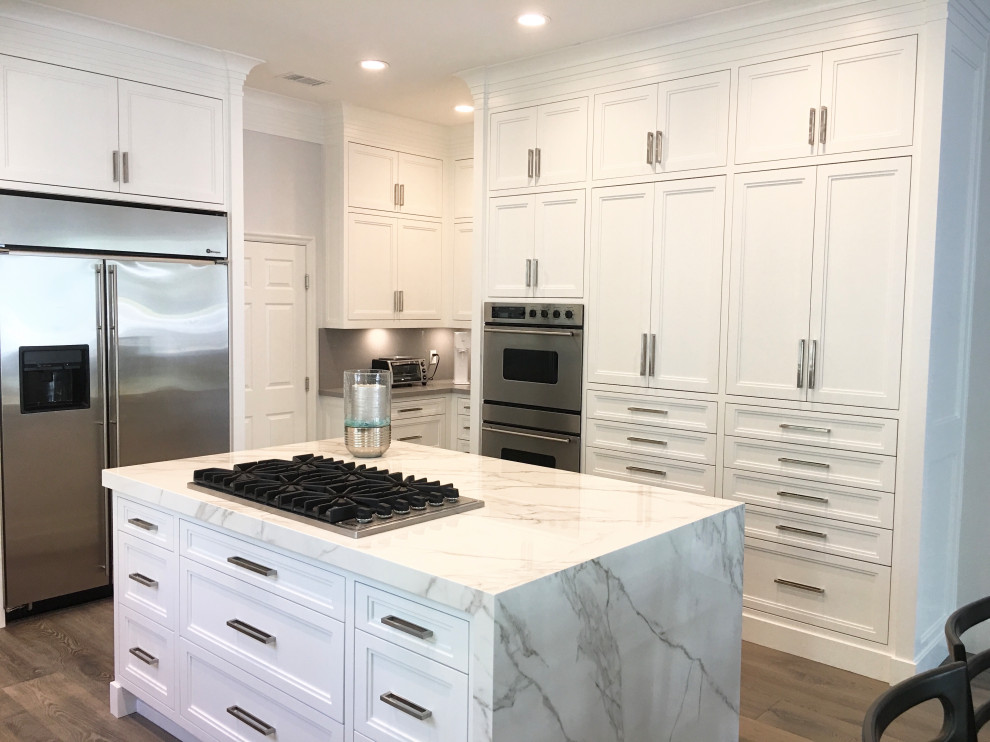 This is an example of a mid-sized contemporary u-shaped open plan kitchen in Los Angeles with an undermount sink, shaker cabinets, white cabinets, quartz benchtops, white splashback, marble splashback, stainless steel appliances, medium hardwood floors, with island, grey floor and white benchtop.
