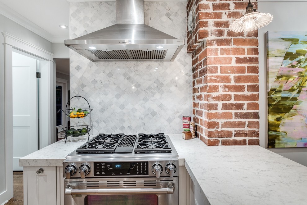 Example of a mid-sized transitional l-shaped medium tone wood floor eat-in kitchen design in Vancouver with a farmhouse sink, shaker cabinets, white cabinets, quartzite countertops, white backsplash, stone tile backsplash, stainless steel appliances and a peninsula