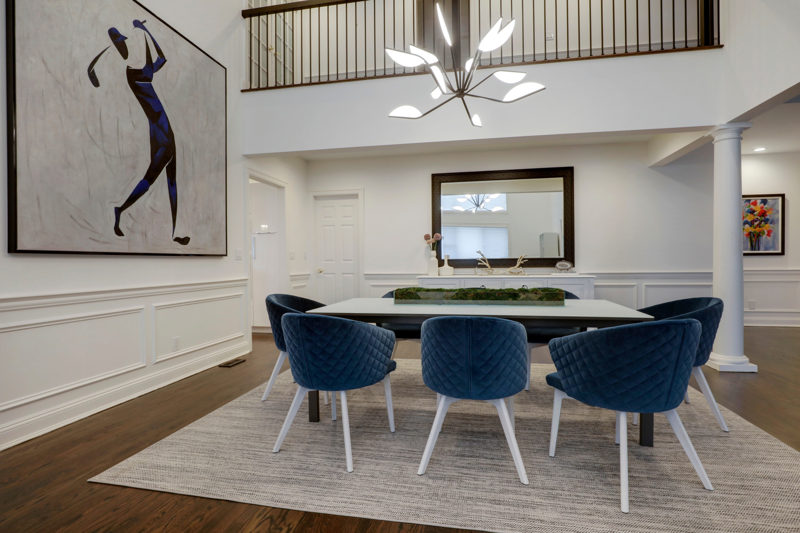The geometric bright chandelier mimics the club in the large painting adding movement and light to the room. The blue quilted chairs with white legs further mimic the painting with the golfers' legs b