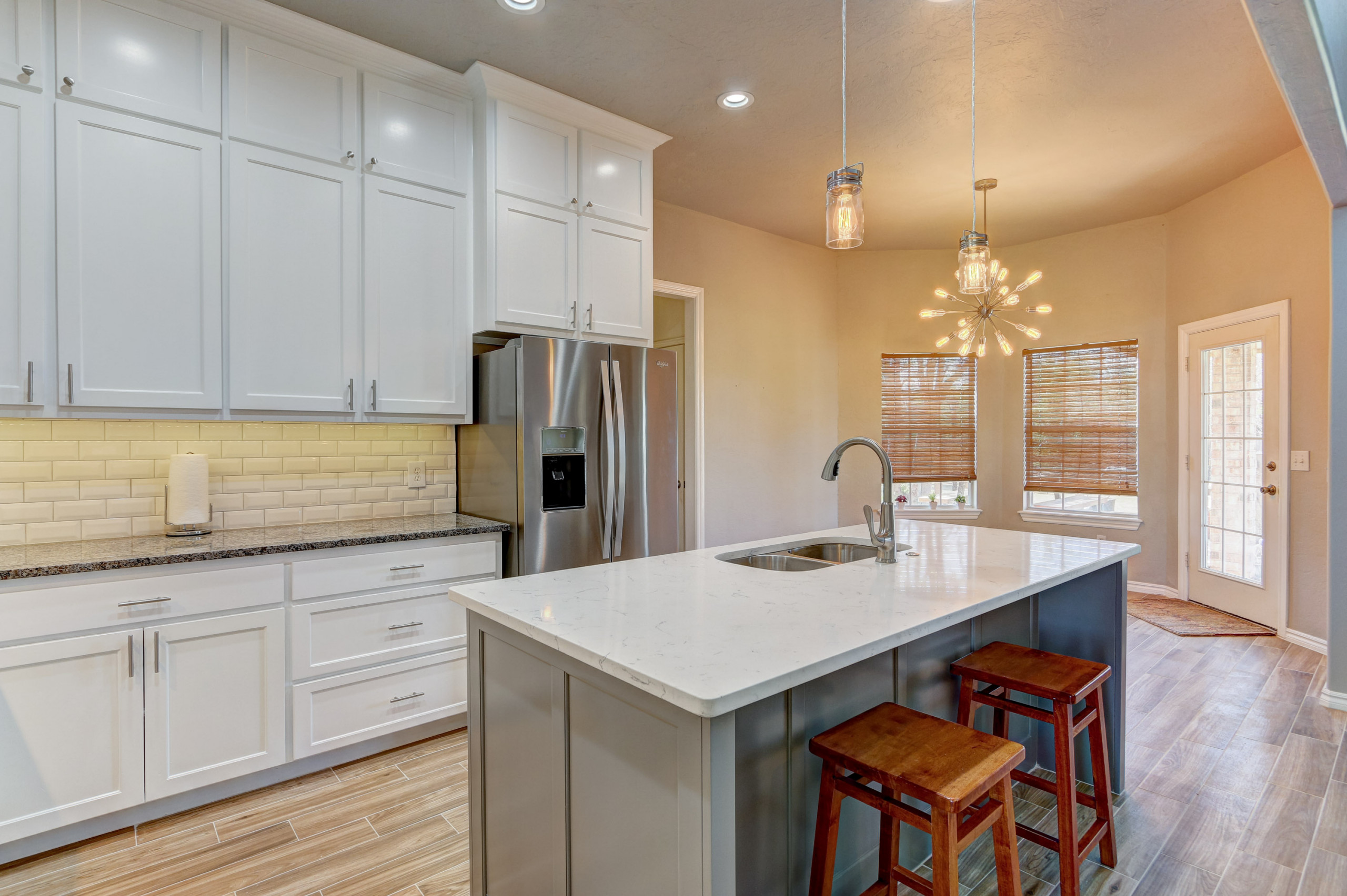 Mid-sized elegant l-shaped cement tile floor kitchen photo in Oklahoma City with an undermount sink, shaker cabinets, white cabinets, quartz countertops, white backsplash, porcelain backsplash, stainl