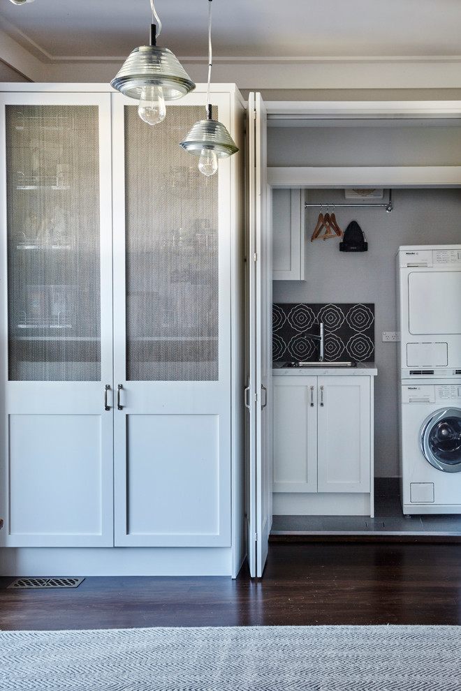 Small traditional single-wall laundry cupboard in Sydney with a single-bowl sink, shaker cabinets, white cabinets, white walls, ceramic floors and a stacked washer and dryer.