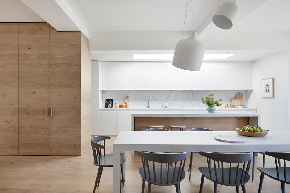 This is an example of a contemporary eat-in kitchen in Melbourne with a double-bowl sink, flat-panel cabinets, white cabinets, grey splashback, stone slab splashback, light hardwood floors, with island, brown floor and grey benchtop.