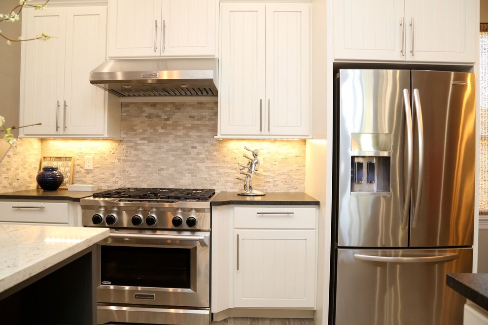 Small transitional u-shaped light wood floor open concept kitchen photo in Orange County with an undermount sink, louvered cabinets, white cabinets, solid surface countertops, beige backsplash, stone tile backsplash, stainless steel appliances and two islands