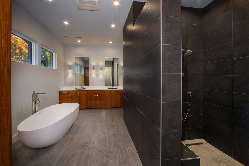 Inspiration for a mid-sized midcentury master bathroom in Dallas with flat-panel cabinets, medium wood cabinets, a freestanding tub, a corner shower, black tile, porcelain tile, grey walls, porcelain floors, a vessel sink, grey floor and an open shower.