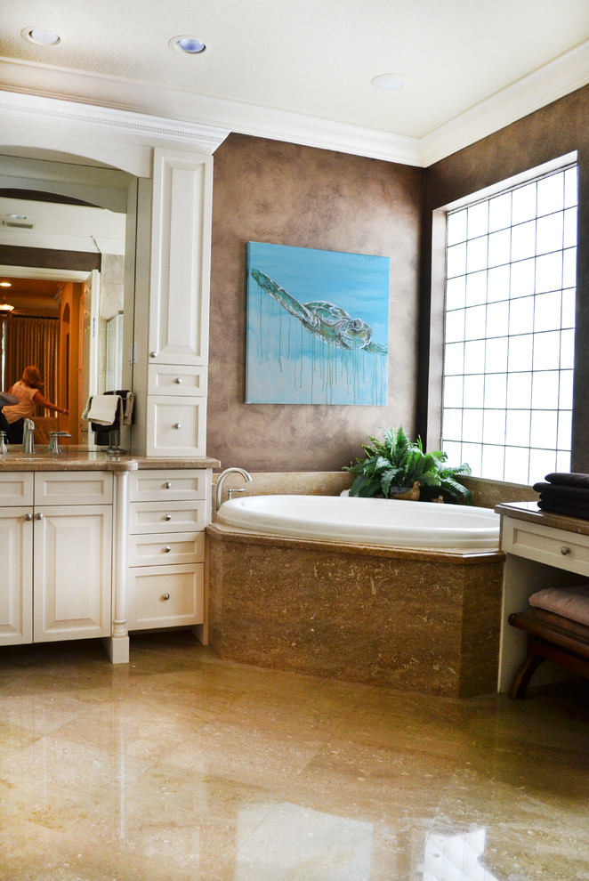 This is an example of a large tropical bathroom in Miami with a drop-in sink, raised-panel cabinets, white cabinets, granite benchtops, a corner tub, a double shower, stone tile and multi-coloured walls.
