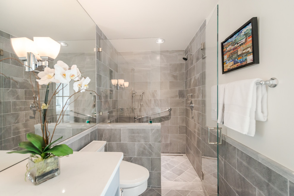 Inspiration for a mid-sized transitional master bathroom in Boston with an alcove shower, a one-piece toilet, gray tile, porcelain tile, grey walls, porcelain floors, solid surface benchtops, grey floor and a hinged shower door.