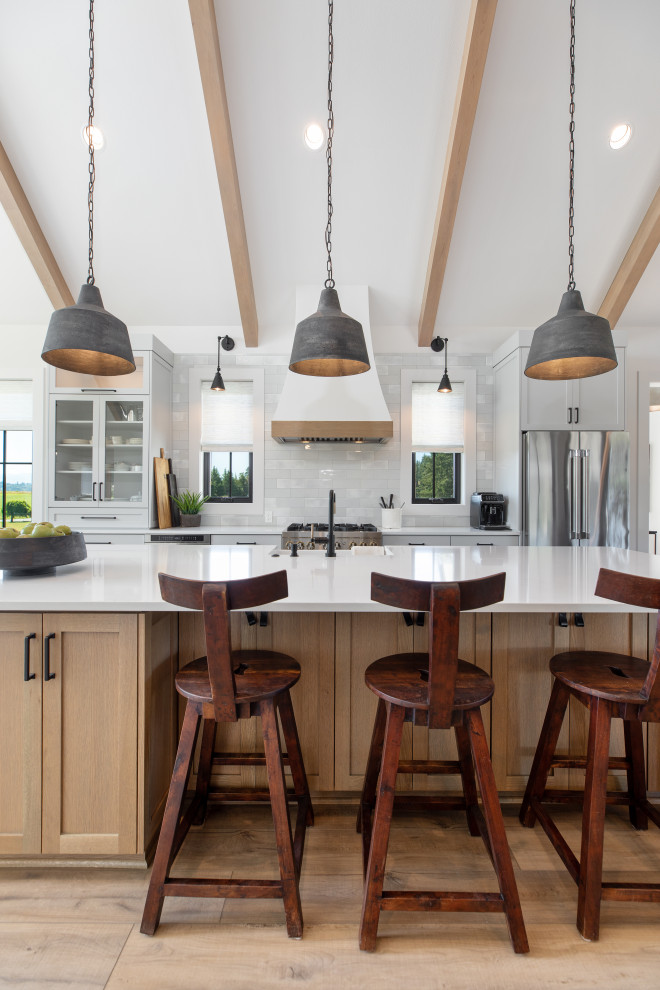 Expansive farmhouse galley kitchen/diner in Portland with a belfast sink, shaker cabinets, white cabinets, engineered stone countertops, white splashback, mosaic tiled splashback, stainless steel appliances, vinyl flooring, an island, brown floors, white worktops and exposed beams.