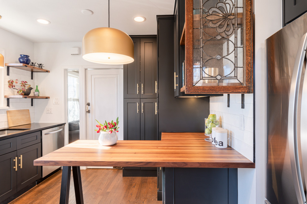 Inspiration for a small contemporary galley separate kitchen in Denver with an undermount sink, shaker cabinets, black cabinets, quartzite benchtops, white splashback, ceramic splashback, stainless steel appliances, dark hardwood floors, a peninsula, brown floor and black benchtop.