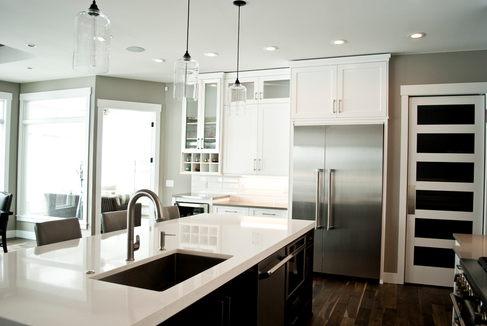 Example of a transitional kitchen design with recessed-panel cabinets, white cabinets, quartz countertops, white backsplash, stainless steel appliances and an island