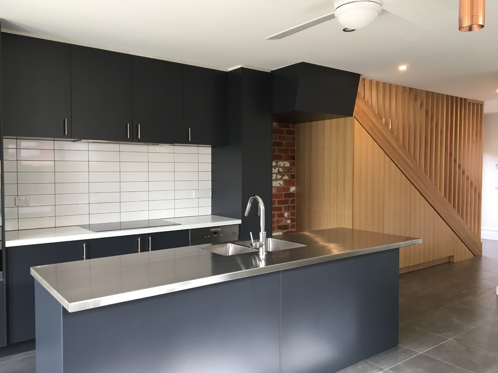 Mid-sized contemporary galley eat-in kitchen in Melbourne with a drop-in sink, flat-panel cabinets, blue cabinets, stainless steel benchtops, white splashback, ceramic splashback, stainless steel appliances, ceramic floors, with island, grey floor and blue benchtop.