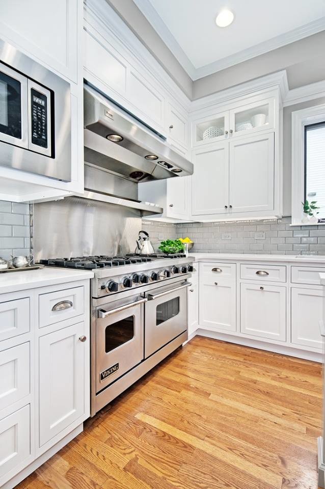 Mid-sized transitional l-shaped light wood floor and beige floor kitchen photo in Chicago with an undermount sink, shaker cabinets, white cabinets, quartzite countertops, gray backsplash, subway tile backsplash, stainless steel appliances and an island