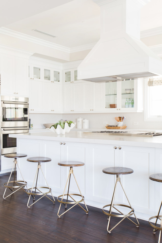 This is an example of a transitional u-shaped open plan kitchen in Los Angeles with white cabinets, white splashback, stainless steel appliances, dark hardwood floors, with island and shaker cabinets.