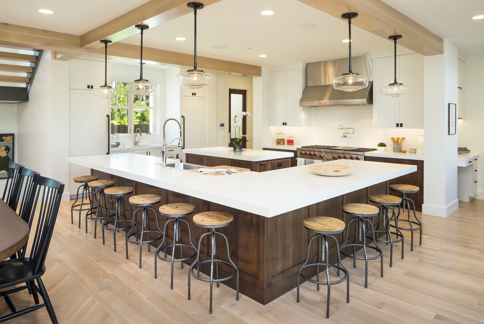 This is an example of an expansive arts and crafts kitchen in Salt Lake City with a farmhouse sink, marble benchtops, white splashback, ceramic splashback, stainless steel appliances, light hardwood floors, multiple islands, beige floor and white benchtop.