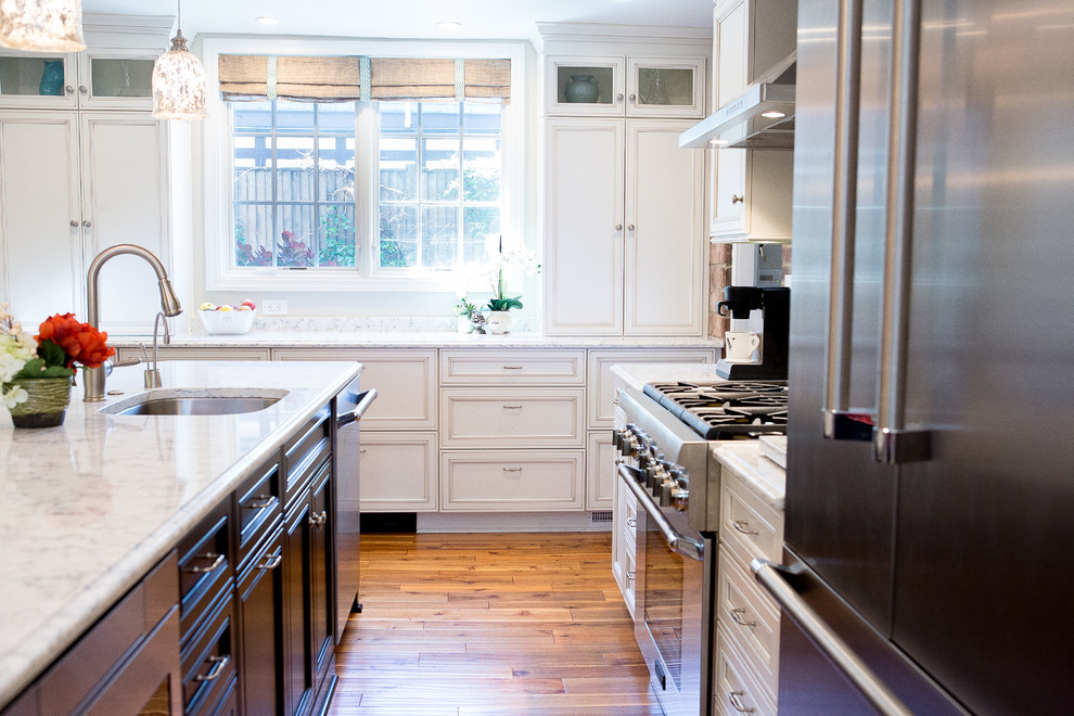 Large transitional medium tone wood floor eat-in kitchen photo with an undermount sink, recessed-panel cabinets, black cabinets, quartz countertops, brick backsplash, stainless steel appliances and an island