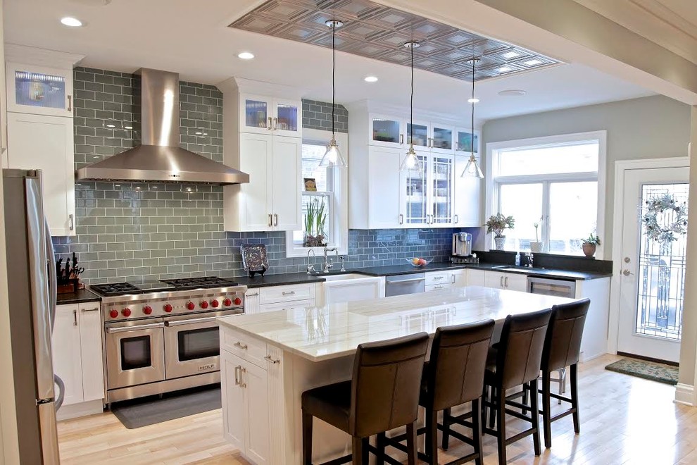 Example of a mid-sized transitional u-shaped light wood floor open concept kitchen design in Chicago with a farmhouse sink, shaker cabinets, white cabinets, quartzite countertops, green backsplash, stainless steel appliances, an island and subway tile backsplash