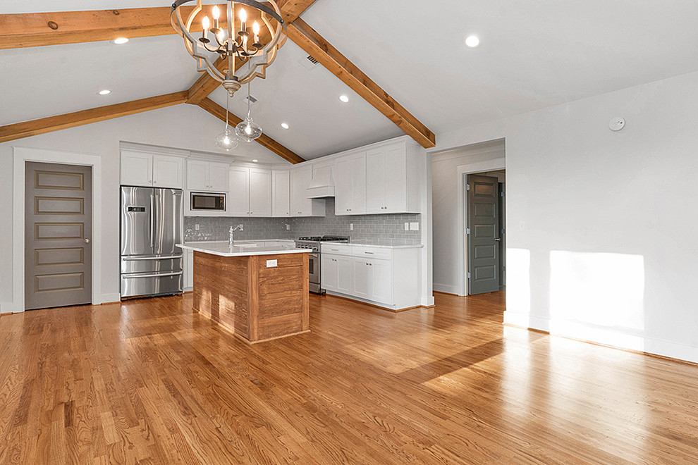Example of a mid-sized transitional l-shaped medium tone wood floor and brown floor open concept kitchen design in Birmingham with a farmhouse sink, shaker cabinets, white cabinets, marble countertops, gray backsplash, subway tile backsplash, stainless steel appliances, an island and white countertops