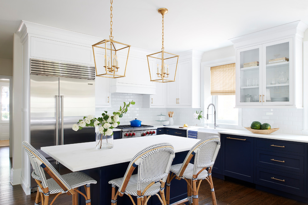 Mid-sized beach style l-shaped kitchen in Philadelphia with a farmhouse sink, white splashback, subway tile splashback, stainless steel appliances, dark hardwood floors, with island, brown floor, white benchtop, recessed-panel cabinets and blue cabinets.