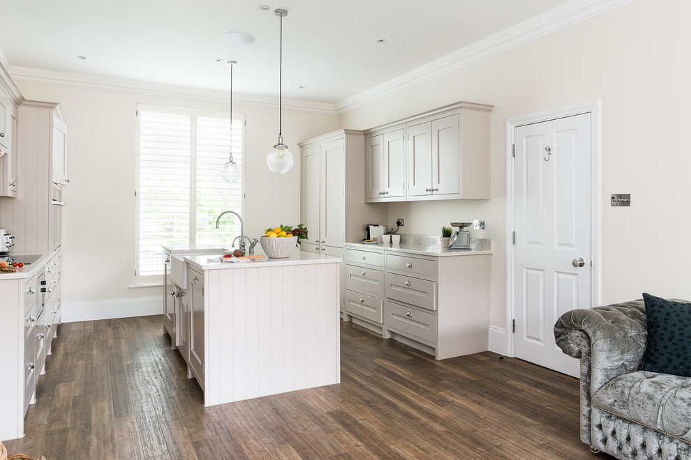Photo of a large traditional kitchen/diner in London with a belfast sink, shaker cabinets, beige cabinets, granite worktops, medium hardwood flooring, an island and white worktops.