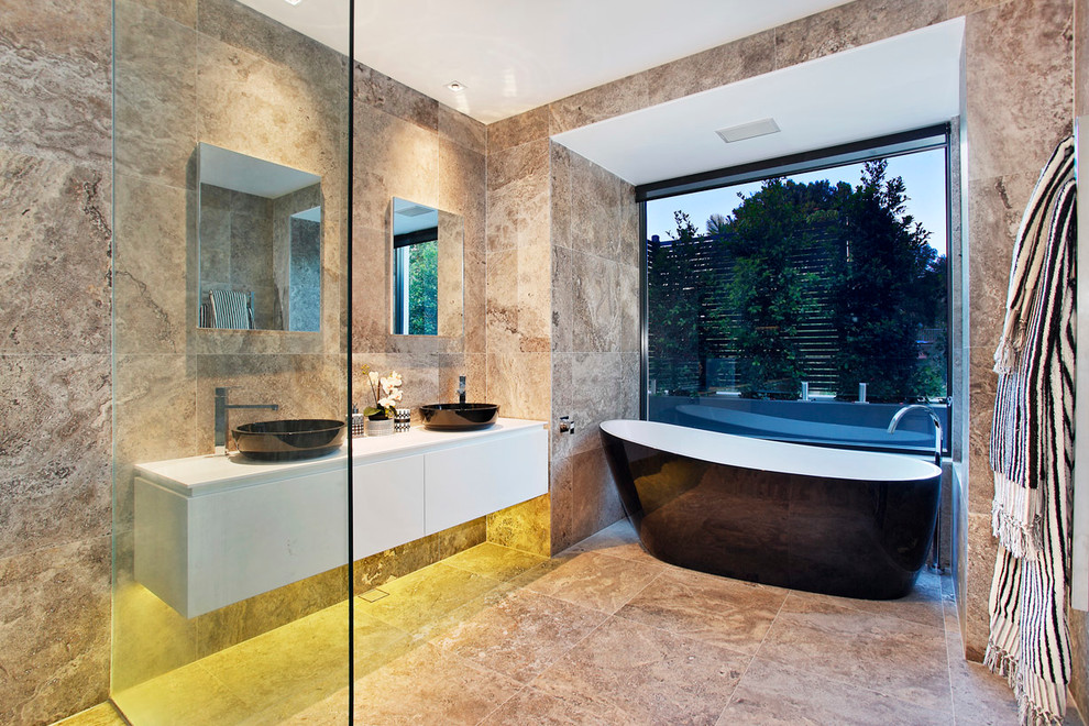 Design ideas for a large contemporary bathroom in Sydney with a vessel sink, flat-panel cabinets, white cabinets, solid surface benchtops, a freestanding tub, an open shower, a wall-mount toilet, beige tile, beige walls, travertine floors, an open shower and travertine.