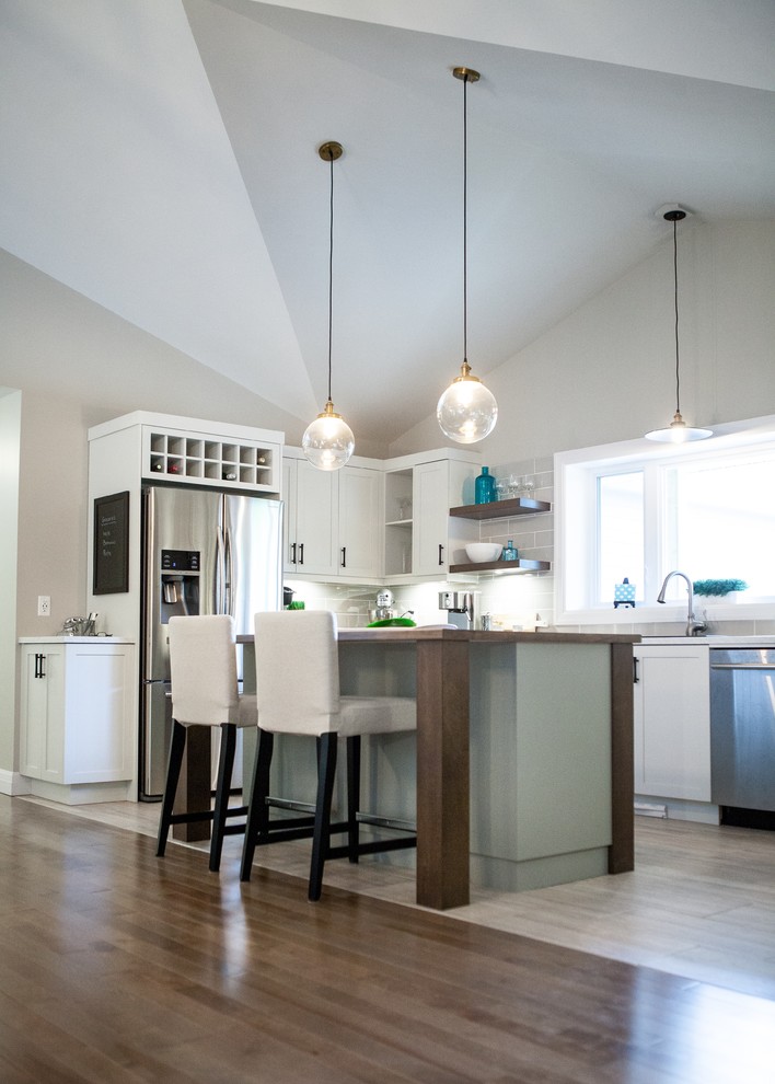 Example of a mid-sized minimalist u-shaped medium tone wood floor and brown floor open concept kitchen design with a drop-in sink, shaker cabinets, white cabinets, quartz countertops, gray backsplash, ceramic backsplash, stainless steel appliances, an island and white countertops