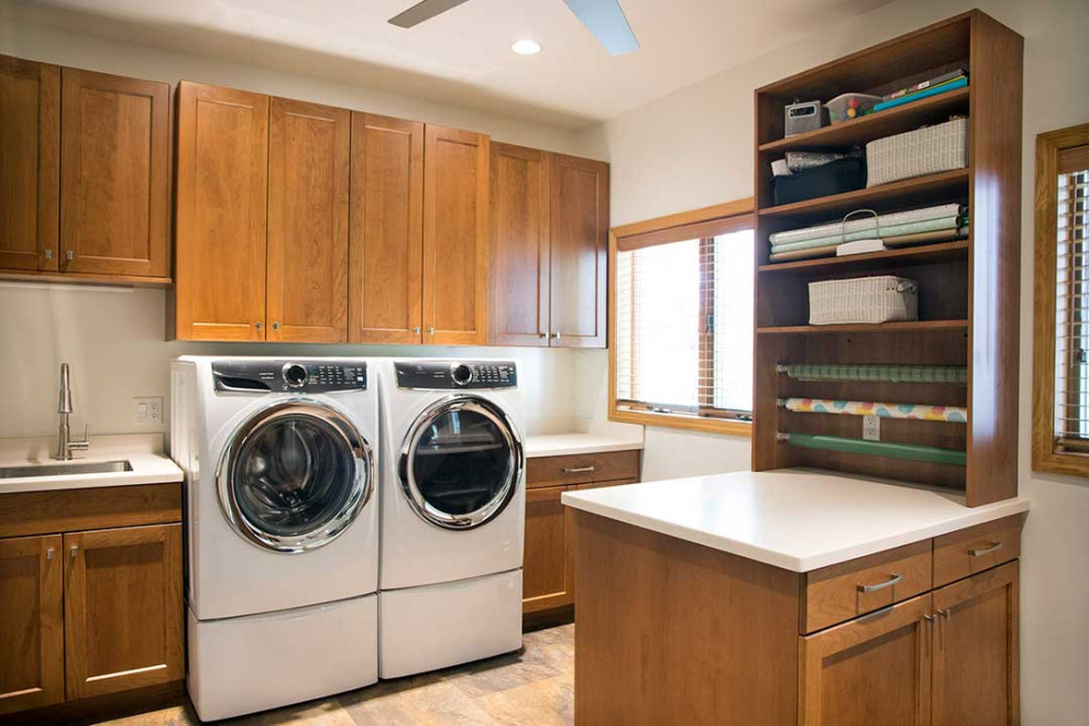 This is an example of a large transitional single-wall utility room in Other with an undermount sink, shaker cabinets, medium wood cabinets, solid surface benchtops, beige walls, ceramic floors, a side-by-side washer and dryer, beige floor and white benchtop.