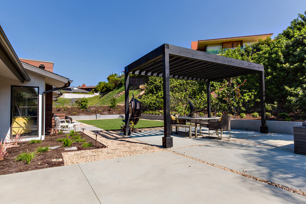 This is an example of a contemporary backyard patio in San Diego with a fire feature, concrete slab and an awning.