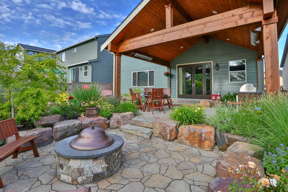 This is an example of a large arts and crafts backyard patio in Seattle with a fire feature, concrete pavers and a roof extension.