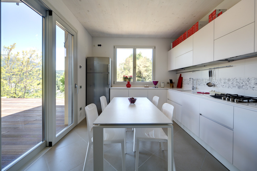 Inspiration for a mid-sized contemporary l-shaped eat-in kitchen in Milan with a double-bowl sink, flat-panel cabinets, white cabinets, granite benchtops, white splashback, ceramic splashback, stainless steel appliances and porcelain floors.