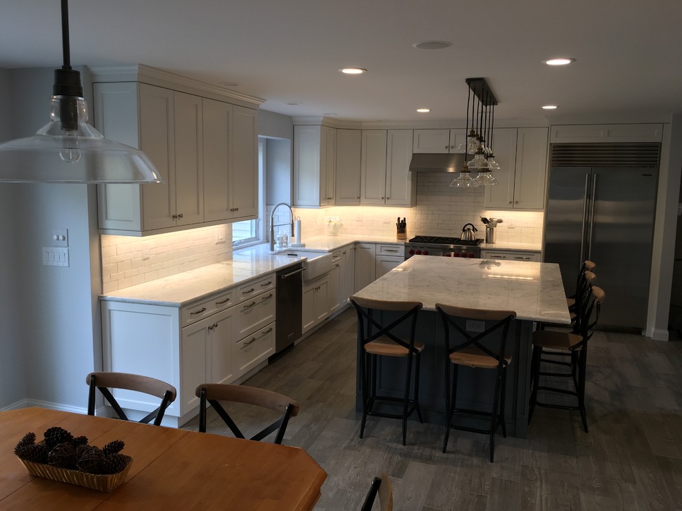 Design ideas for a large country l-shaped eat-in kitchen in New York with a farmhouse sink, recessed-panel cabinets, white cabinets, quartzite benchtops, white splashback, ceramic splashback, stainless steel appliances, porcelain floors and with island.