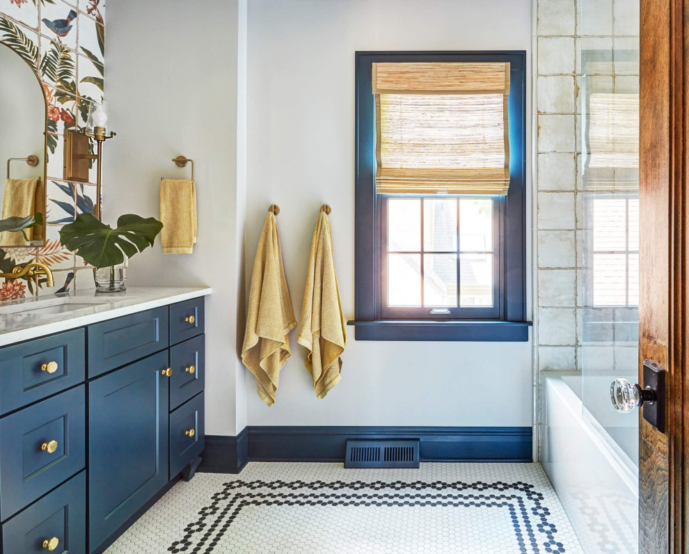 This is an example of a mid-sized tropical master bathroom in Other with beaded inset cabinets, blue cabinets, a drop-in tub, a shower/bathtub combo, white tile, ceramic tile, multi-coloured walls, mosaic tile floors, a drop-in sink, marble benchtops, multi-coloured floor, a shower curtain, white benchtops, a single vanity, a freestanding vanity and wallpaper.