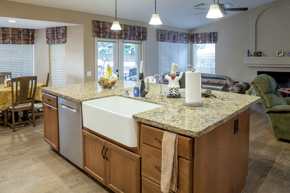 Example of a mid-sized transitional l-shaped laminate floor and brown floor open concept kitchen design in Phoenix with a farmhouse sink, recessed-panel cabinets, medium tone wood cabinets, granite countertops, beige backsplash, stone slab backsplash, stainless steel appliances and an island