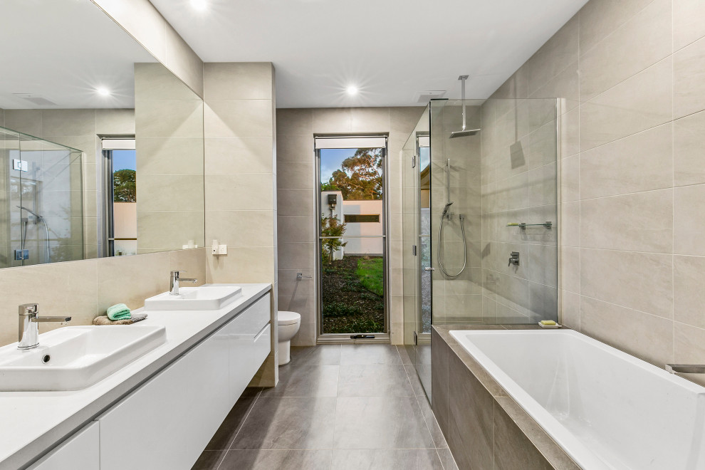 Inspiration for a contemporary bathroom in Melbourne with flat-panel cabinets, white cabinets, a drop-in tub, a corner shower, beige tile, a drop-in sink, grey floor, a hinged shower door, white benchtops, a double vanity and a floating vanity.