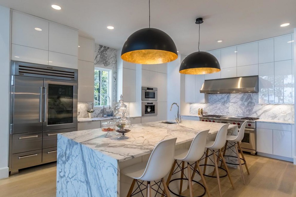 This is an example of a contemporary l-shaped kitchen with an undermount sink, flat-panel cabinets, white cabinets, quartz benchtops, grey splashback, stone slab splashback, stainless steel appliances, light hardwood floors, with island and beige floor.
