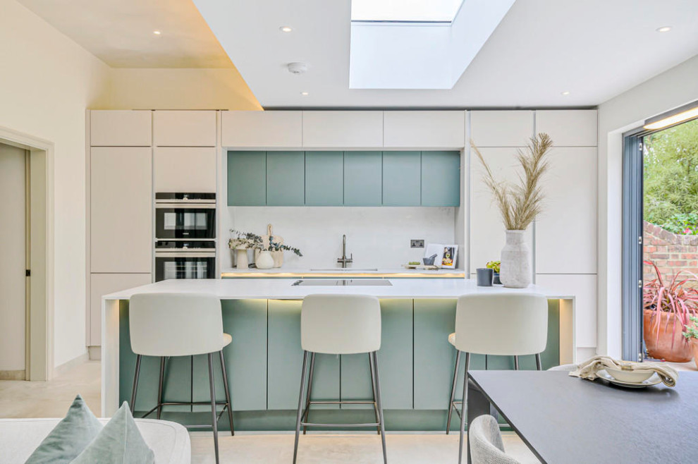 Photo of a medium sized modern grey and teal single-wall open plan kitchen in London with a single-bowl sink, flat-panel cabinets, green cabinets, quartz worktops, white splashback, marble splashback, stainless steel appliances, cement flooring, an island, beige floors, white worktops, a coffered ceiling and feature lighting.