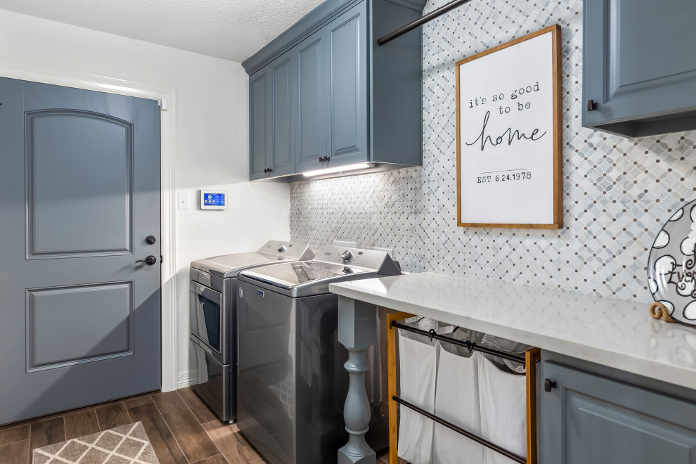 Inspiration for a transitional dedicated laundry room in Houston with raised-panel cabinets, grey cabinets, white walls, a side-by-side washer and dryer, brown floor and white benchtop.