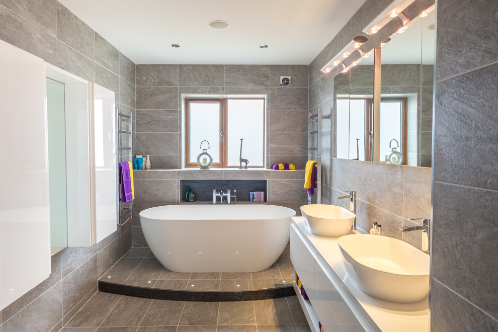 Contemporary master bathroom in Other with flat-panel cabinets, white cabinets, a freestanding tub, gray tile, grey walls, a vessel sink, grey floor and white benchtops.