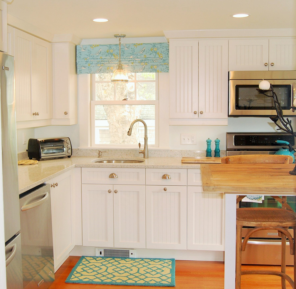 Photo of a beach style l-shaped separate kitchen in Boston with an undermount sink, white cabinets, recycled glass benchtops, stainless steel appliances, medium hardwood floors, no island and shaker cabinets.