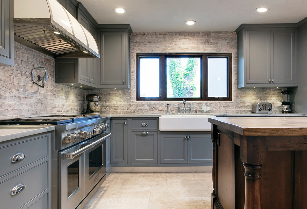 Inspiration for a large traditional l-shaped separate kitchen in Albuquerque with recessed-panel cabinets, grey cabinets, with island, a farmhouse sink, marble benchtops, brown splashback, brick splashback, stainless steel appliances and limestone floors.