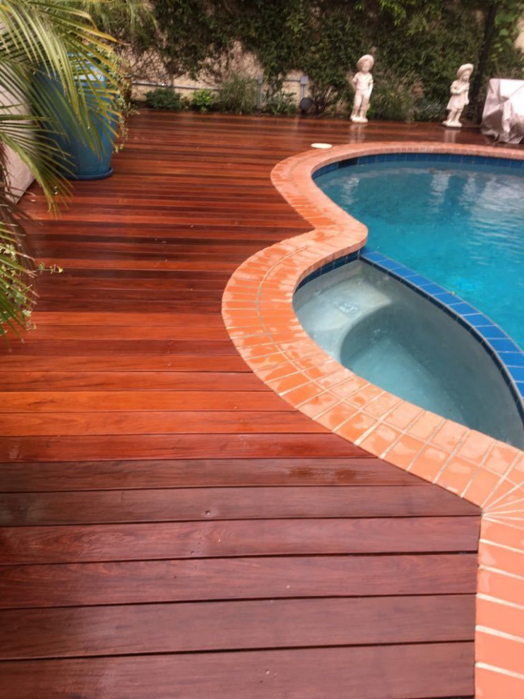 Cette photo montre un piscine avec aménagement paysager arrière moderne en forme de haricot de taille moyenne avec une terrasse en bois.