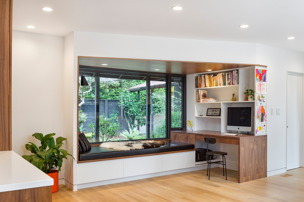 This is an example of a mid-sized midcentury study room in Portland with white walls, light hardwood floors, no fireplace, a built-in desk and beige floor.