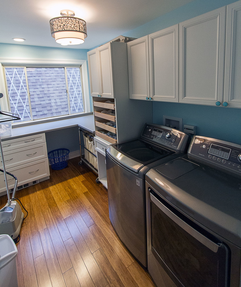 Photo of a mid-sized contemporary l-shaped dedicated laundry room in Other with an undermount sink, recessed-panel cabinets, white cabinets, quartz benchtops, blue walls, bamboo floors and a side-by-side washer and dryer.