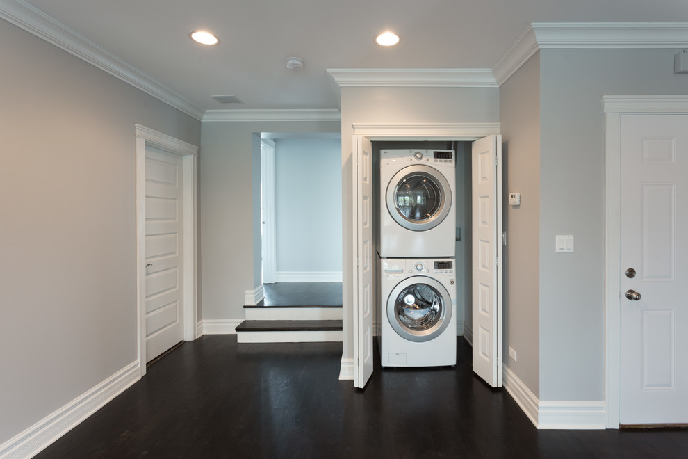 Design ideas for a mid-sized contemporary galley utility room in Chicago with dark hardwood floors, a stacked washer and dryer, brown floor and grey walls.