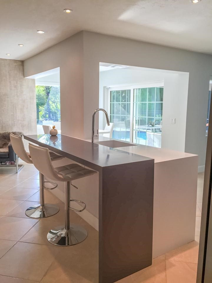 Inspiration for a mid-sized modern l-shaped open plan kitchen in Miami with solid surface benchtops, an integrated sink, flat-panel cabinets, medium wood cabinets, white splashback, stone slab splashback, stainless steel appliances, ceramic floors, with island, beige floor and grey benchtop.