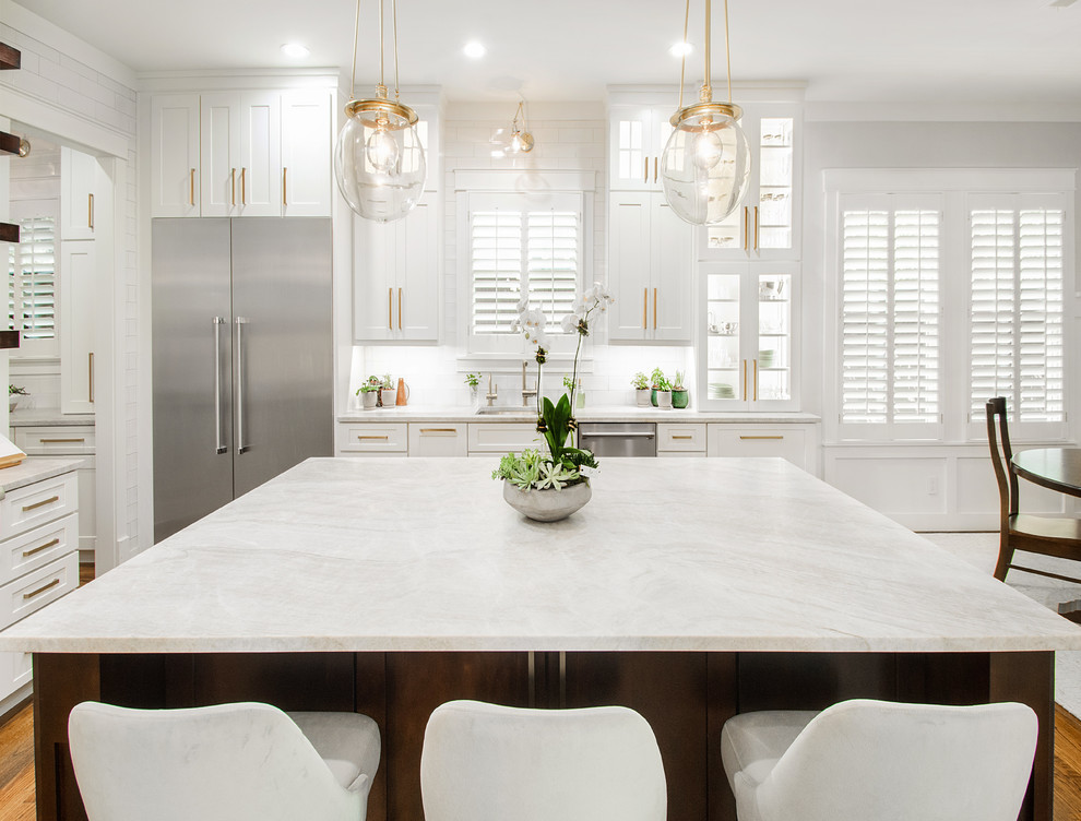 This is an example of a large transitional l-shaped open plan kitchen in Dallas with a drop-in sink, flat-panel cabinets, white cabinets, quartzite benchtops, white splashback, ceramic splashback, stainless steel appliances, dark hardwood floors, with island, brown floor and grey benchtop.