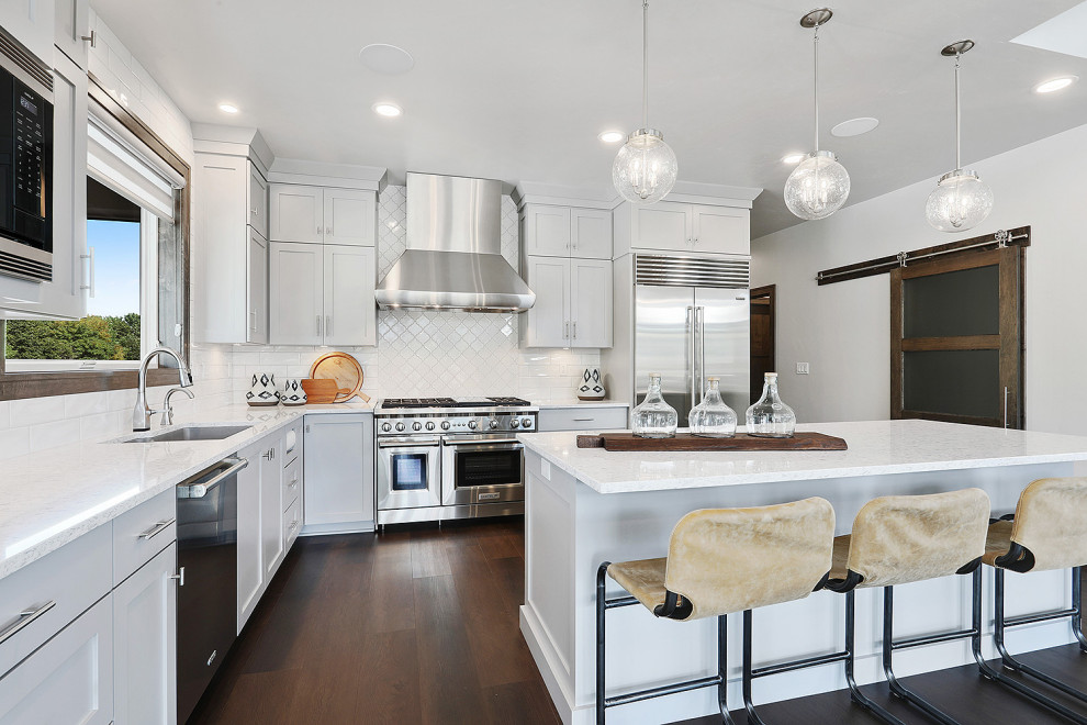 Inspiration for a mid-sized transitional u-shaped vinyl floor and brown floor open concept kitchen remodel with an undermount sink, flat-panel cabinets, gray cabinets, quartz countertops, white backsplash, porcelain backsplash, stainless steel appliances, an island and white countertops