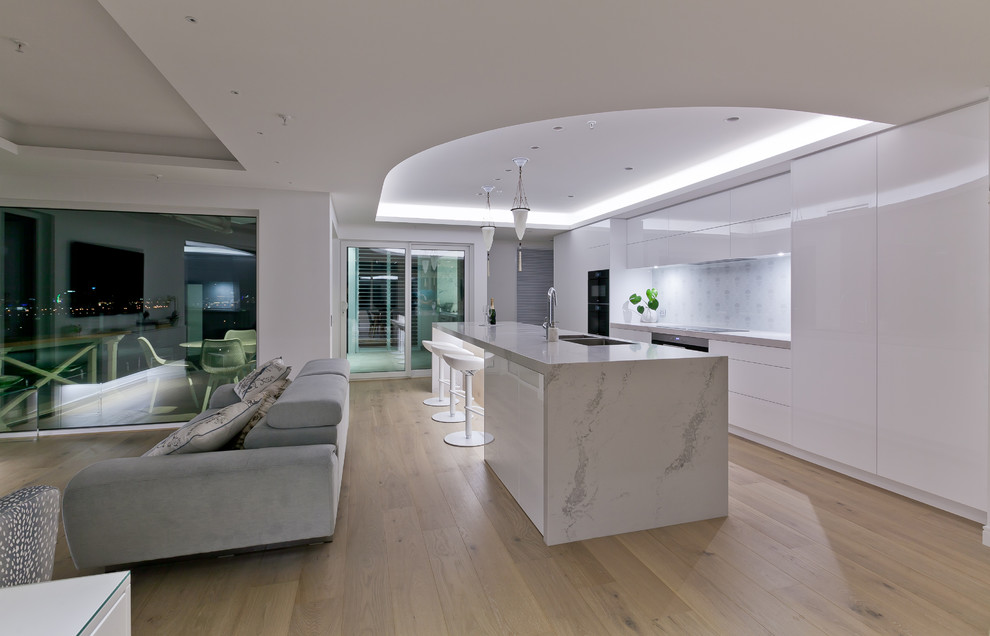 Inspiration for a large contemporary galley open plan kitchen in Perth with an undermount sink, flat-panel cabinets, white cabinets, quartz benchtops, white splashback, porcelain splashback, stainless steel appliances, light hardwood floors, with island and white benchtop.